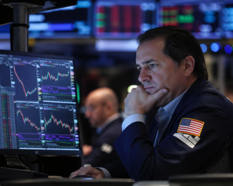 A trader studies multiple market charts on computer screens in a dimly lit trading floor, reflecting cautious sentiment in global equity markets.