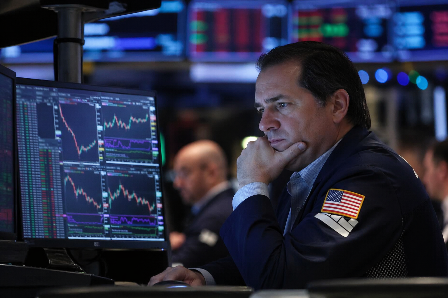 A trader studies multiple market charts on computer screens in a dimly lit trading floor, reflecting cautious sentiment in global equity markets.