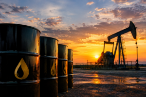 Black oil barrels in the foreground with an operating oil pumpjack at sunset, symbolizing rising crude oil prices and global energy market supply concerns.